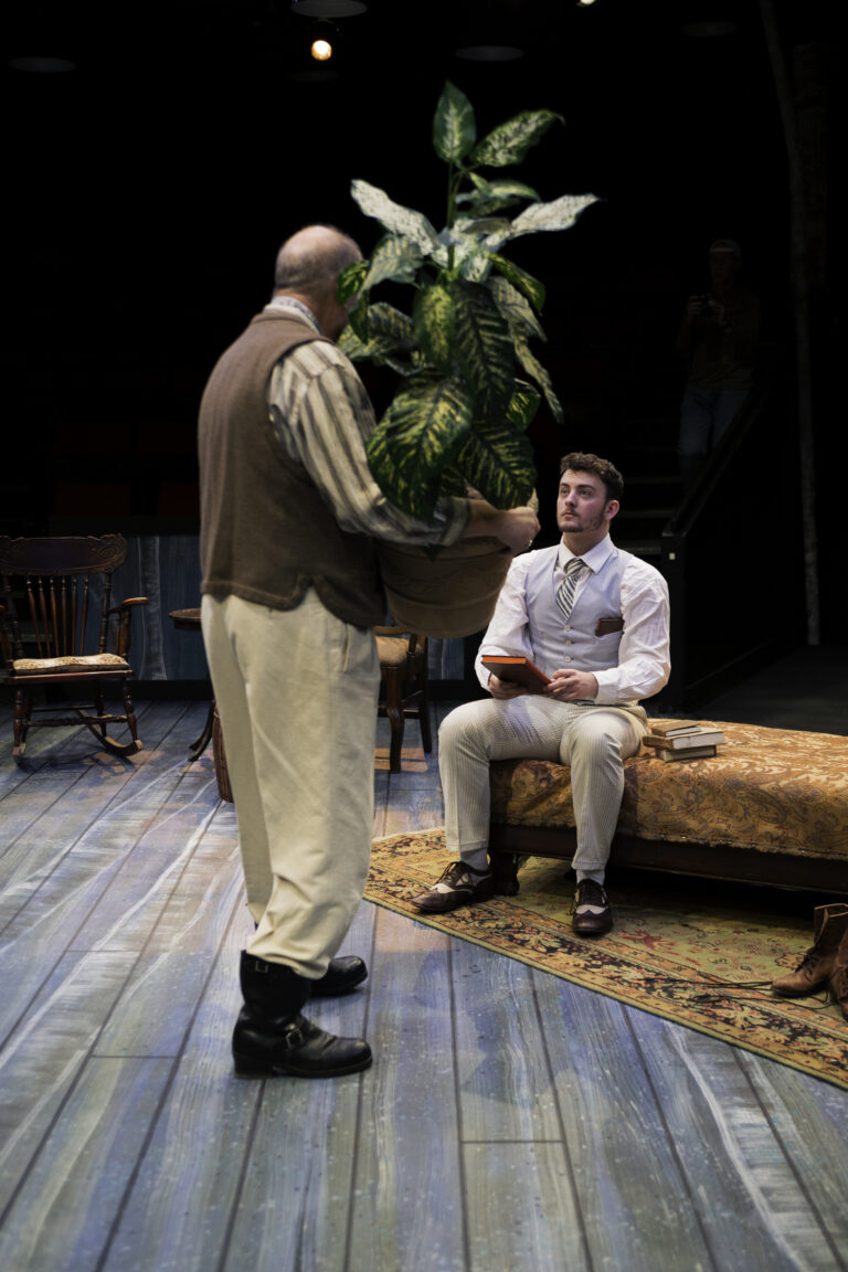 Production photo from The Seagull Man in Russian costume holding a large plant