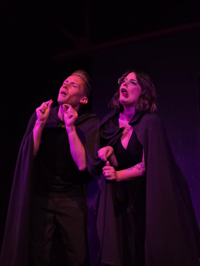 Photo of man and woman making silly faces with elven cloaks on.